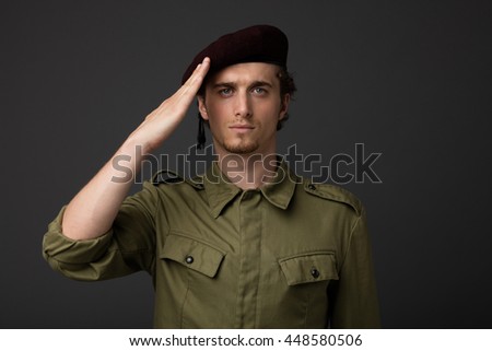young military with red beret and green uniform on gray background, salute