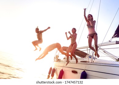 Young millenial friends jumping from sailboat at sea ocean trip - Guys and girls having summer fun together at sail boat party day - Luxury excursion concept on bright vivid filter with soft focus