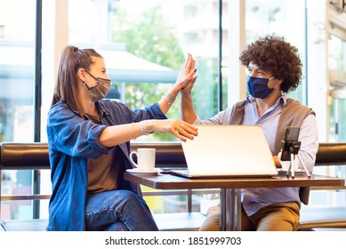 Young Millenial Students Giving Each Other An High Five After Done Studying And Video Calling On A Smartphone Wearing Protective Face Mask. Concept About New Influencer, Tech And Smart Work In Startup