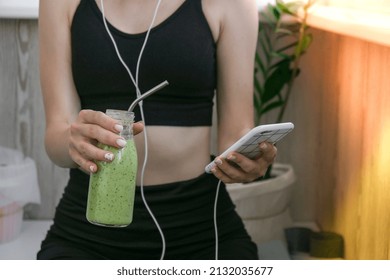 Young millenial woman checking smartphone drinking vegan smoothie drink detox. Woman doing yoga exercises at home. Online tuition Clean eating, weight loss, healthy dieting food concept. Stay healthy