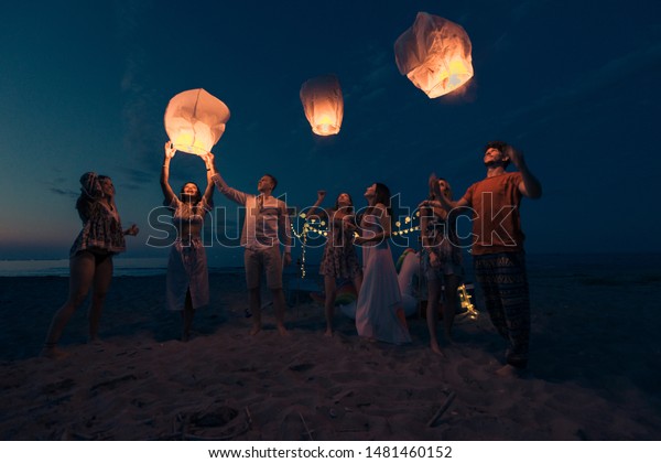 Young millenials holding and igniting sky\
lantern - Lantern festival on the\
beach