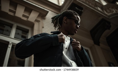 Young Millennial African Boy In City. Happy Black Man In Jacket With Camera. Generation Z Concept.  Man Walking On The Street.Portrait Of Pensive Modern Afro Man With Sunglasses And Camera