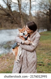 Young Millennial Beautiful Woman Brunette Is Walking With Her Japanese Breed Shiba Inu Dog Outdoor Near The Riverside Bank On A Leash.