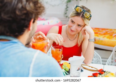 A Young Millennial Couple In Love Drinking Cocktails Together, Enjoying Summer Day In Beach Cafe - Blonde Hair Girl Looking To Her Boyfriend And Flirting