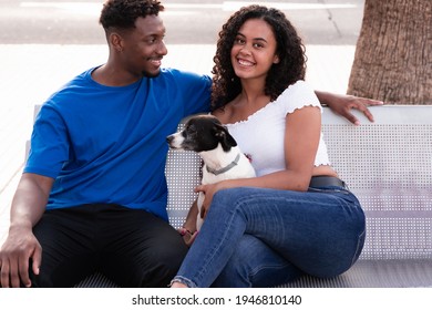 Young Millennial Couple With Their Dog. Young Friends And Dog Sitting On A Bench, Waiting For Other Friends. Love, Friendship And Pet Concept.