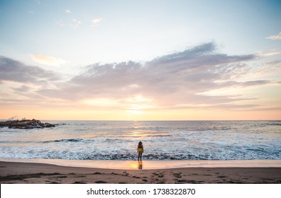 Young millennial female backpacker standing at the edge of the shoreline watching sunset over the Pacific Ocean in Las Peñitas, Nicaragua
