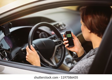 Young Millennial Woman Using Breath Alcohol Analyzer In The Car. Closeup With Selective Focus. Girl Taking Alcohol Test With Breathalyzer.