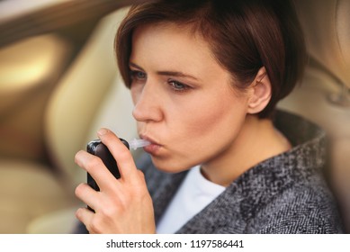 Young Millennial Woman Using Breath Alcohol Analyzer In The Car. Closeup With Selective Focus. Girl Taking Alcohol Test With Breathalyzer.