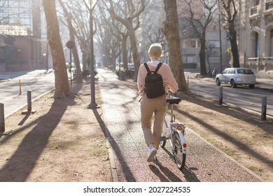 young millennial woman walking down the city street, carrying a bicycle in her hands. Concept of healthy life. Ecological mode of transportation. Horizontal image. Copy space for text.