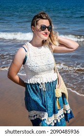 Young Millennial Woman Wearing A Blue And White Paisley Dress, A Beach Bag And Sunglasses While Enjoying A Summer Beach Vacation, Time Off Or A Tranquil Lifestyle, In Tenerife, Canary Islands, Spain