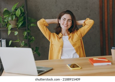 Young minded fun employee business woman 20s wear casual yellow shirt look aside in pensive mood dream hold hands behind neck sit work at wooden office desk with pc laptop Achievement career concept - Powered by Shutterstock