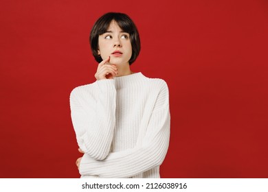 Young Minded Pensive Thoughtful Woman 20s Wear White Knitted Sweater Look Aside On Workspace Area Mock Up Prop Up Chin Isolated On Plain Red Color Background Studio Portrait. People Lifestyle Concept