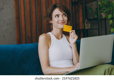 Young Minded Woman Wear White Tank Shirt Using Laptop Pc Computer Credit Bank Card Shopping Online Booking Tour Sit On Blue Sofa Stay Home Flat Rest Relax Spend Free Spare Time In Living Room Indoors