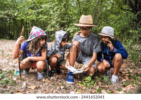 Young minds engrossed in a forest guidebook. A group of children learning and bonding through shared outdoor education and discovery. Multiethnic group of curious happy kids.
