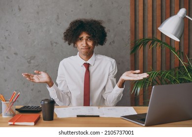 Young Mistaken Confused Uncertain African American Employee Business Man In Classic Shirt Tie Spread Hands Like Oops Gesture Sit Work At White Office Desk With Pc Laptop Achievement Career Concept.