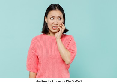 Young mistaken puzzled woman of Asian ethnicity 20s in pink sweater look aside on workspace biting nails fingers isolated on pastel plain light blue background studio portrait People lifestyle concept - Shutterstock ID 2136727063