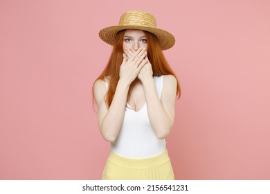 Young mistaken shocked confused caucasian redhead woman ginger long hair wear straw hat summer clothes cover mouth with hands looking camera isolated on pastel pink color background studio portrait
