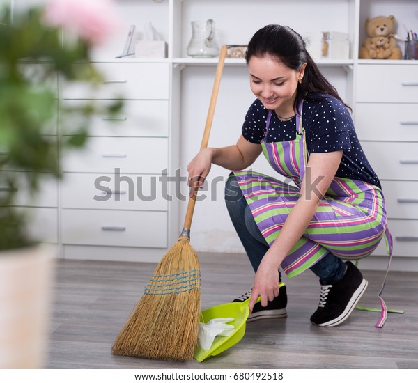 Young mistress sweeping floors in house with broom\
and shovel