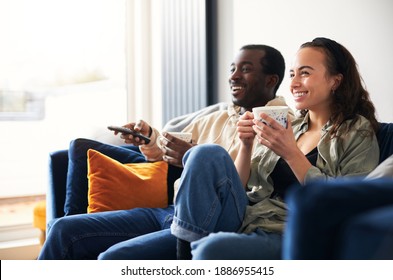 Young Mixed Ethnicity Couple Relaxing On Sofa At Home Watching Or Streaming Tv Together