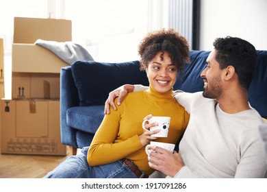 Young Mixed Ethnicity Couple Taking A Break On Moving Day Into New Home Sitting On Floor In Lounge Drinking Coffee Surrounded By Removal Boxes