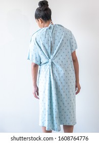 A Young Mixed Race African American Woman Wearing A Hospital Gown Or Robe With Her Back Towards Camera Looks Down And Leans To The Side With Her Arms Limp With A Look Of Discomfort Nausea Or Sadness.