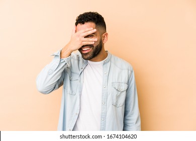 Young Mixed Race Arabic Man Isolated Blink At The Camera Through Fingers, Embarrassed Covering Face.