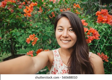 Young mixed race  asian girl with long black hair takes selfie smiling, portrait with flowers