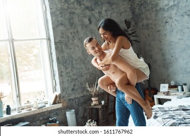 Young mixed race couple boyfriend carrying girlfriend on his back in bedroom at home laughing happy