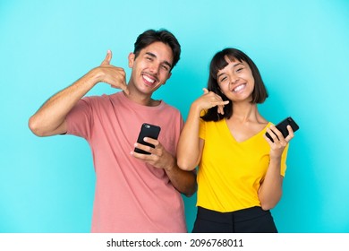 Young Mixed Race Couple Holding Mobile Phone Isolated On Blue Background Making Phone Gesture. Call Me Back Sign