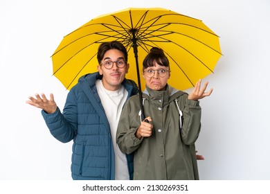 Young mixed race couple holding an umbrella isolated on white background having doubts while raising hands and shoulders - Powered by Shutterstock