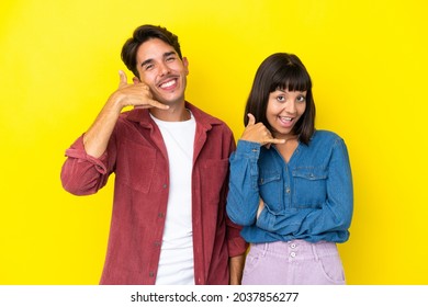 Young Mixed Race Couple Isolated On Yellow Background Making Phone Gesture. Call Me Back Sign