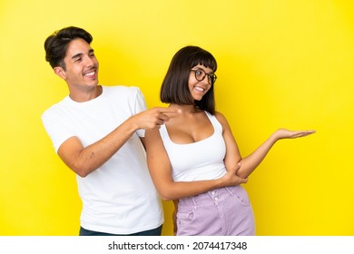 Young Mixed Race Couple Isolated On Yellow Background Pointing Back And Presenting A Product