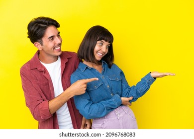 Young Mixed Race Couple Isolated On Yellow Background Pointing Back And Presenting A Product