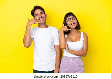 Young Mixed Race Couple Isolated On Yellow Background Making Phone Gesture. Call Me Back Sign