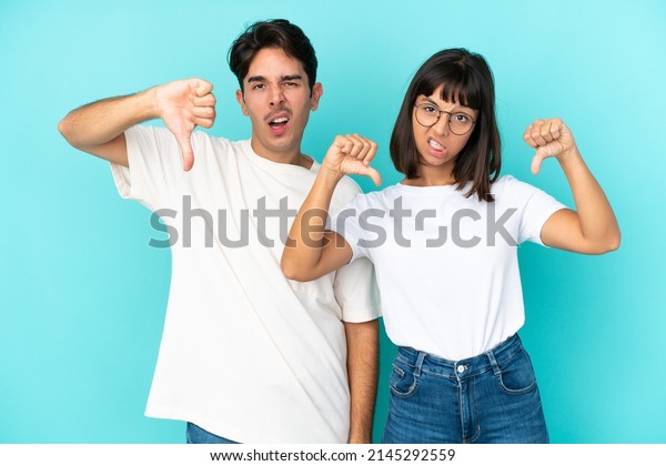 Young mixed race couple isolated on blue\
background showing thumb down with both\
hands