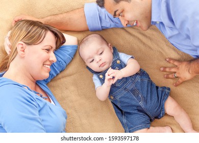 Young Mixed Race Couple Laying With Their Infant On A Blanket.