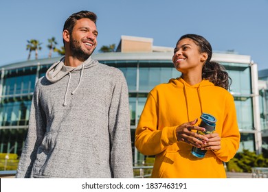 Young Mixed Race Couple Talking During Jogging With Modern Building Behind