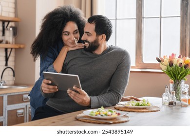 Young mixed race couple using digital tablet while have healthy dinner in light modern kitchen, checking online recipe on internet, ordering food delivery. Love, family and meal with vegetables - Powered by Shutterstock