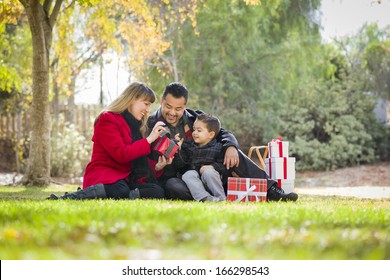 Young Mixed Race Family Enjoying Christmas Gifts In The Park Together.