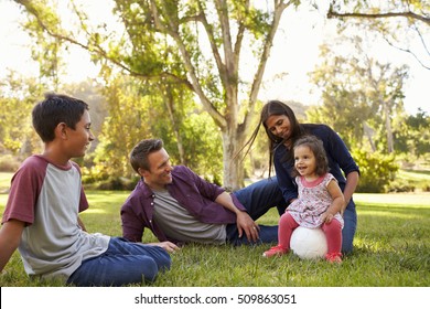 Young Mixed Race Family Relaxing With Soccer Ball In A Park