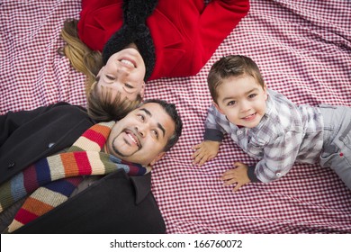 Young Mixed Race Family in Winter Clothing Laying on Their Backs on Picnic Blanket in the Park Together.
