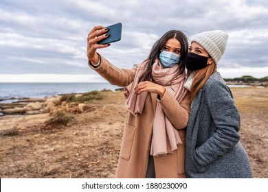 Young Mixed Race Female LGBTQ Couple Making Selfie With Smartphone In Sea Resort In Safe Protection Mask - Hispanic Beautiful Woman Using Tech To Sharing Photo With Her Lesbian Girlfriend On Social