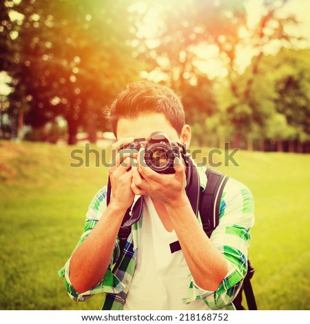 Young mixed race male photographer in park on sunny summer day using digital camera. Square image. Instagram filter look.