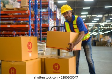 A Young mixed race male worker wearing helmet lifting cardboard box in warehouse, machinery and Logistics concept.  - Powered by Shutterstock