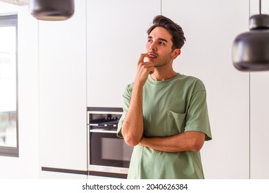 Young mixed race man in his kitchen relaxed thinking about something looking at a copy space.