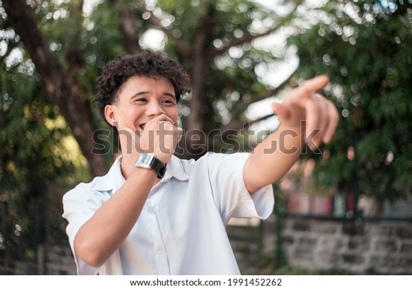An\
young mixed race man points to someone, laughing out loud. Comedic\
situtation or mocking a person. Outdoor\
background.