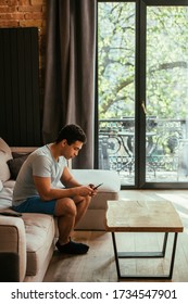 young mixed race man using smartphone on sofa during quarantine