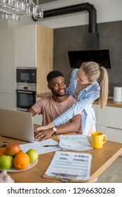 Young Mixed Race Married Couple Having Breakfast At The Morning In Kitchen And Using Laptop. Online Shopping.