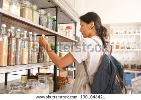 Young Mixed Race Woman Buying Superfoods in Zero Waste Shop. Lots of Healthy Food in Glass Bottles on Stand in Grocery Store. No plastic Conscious Minimalism Vegan Lifestyle Concept.