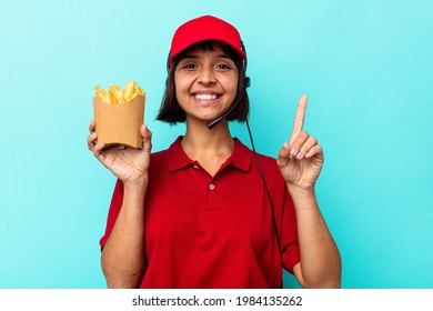 Young Mixed Race Woman Fast Food Restaurant Worker Holding Fries Isolated On Blue Background Showing Number One With Finger.